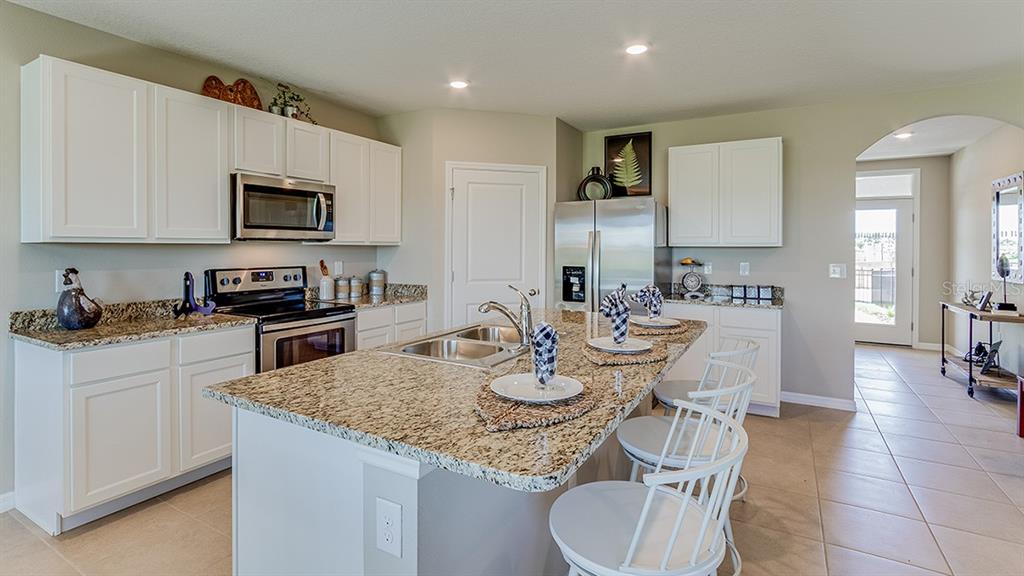 A kitchen features white cabinets, stainless steel appliances, a large island, and light-colored countertops — 10928 RABBIT GROVE TRAIL, PARRISH, FL