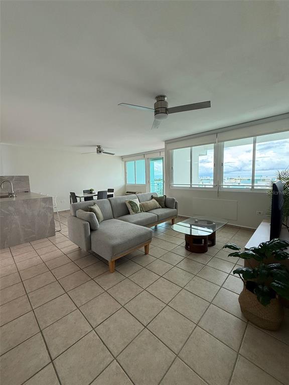 A living room features a grey sectional sofa, tile flooring, and large windows with views — 96QJ+3RG CLL LAS COLINAS UNIT 301, RIO GRANDE, PR