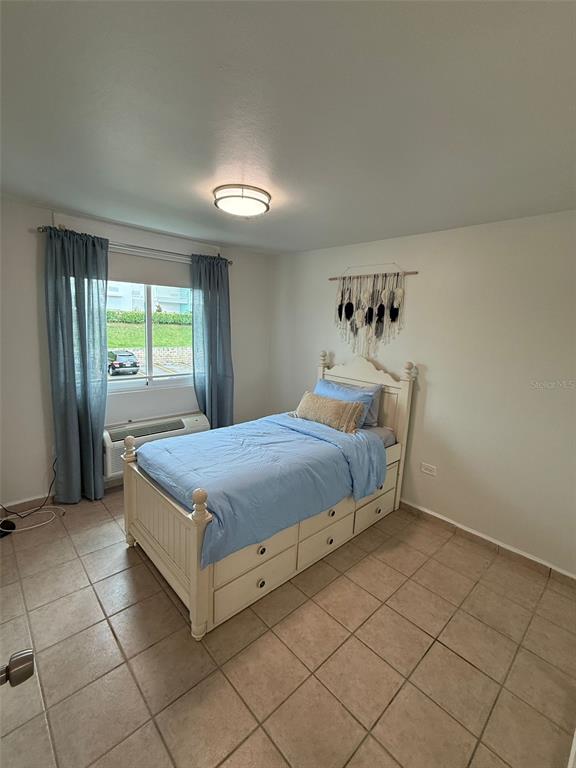 A bedroom features a single bed with storage drawers, tile flooring, and blue curtains — 96QJ+3RG CLL LAS COLINAS UNIT 301, RIO GRANDE, PR