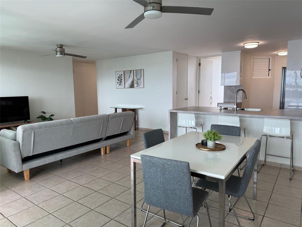 An open-concept living and dining area features tile flooring, a gray sofa, and kitchen island — 96QJ+3RG CLL LAS COLINAS UNIT 301, RIO GRANDE, PR