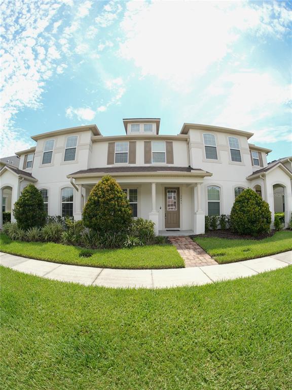 A two-story townhouse with a beige stucco exterior, a covered front porch, and landscaping — 2451 VARENNA LOOP, KISSIMMEE, FL