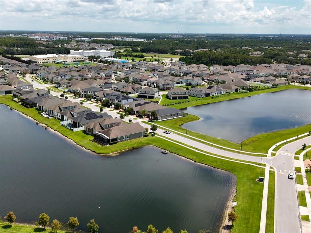 An aerial view shows a suburban neighborhood with houses surrounding a large retention pond — 2451 VARENNA LOOP, KISSIMMEE, FL
