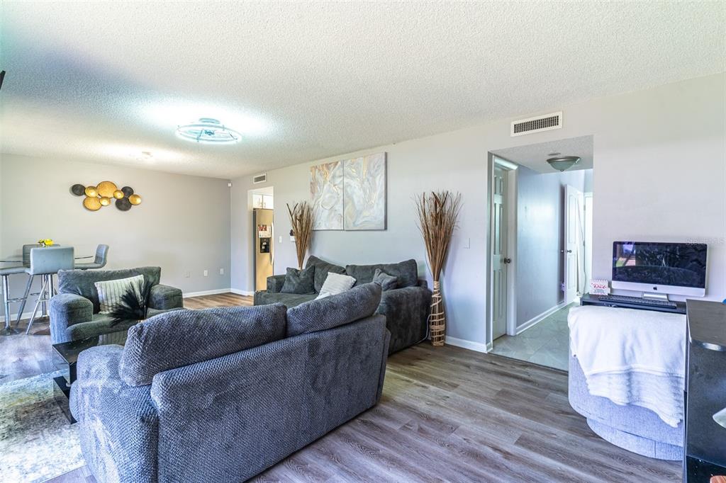 A living room features gray sofas, wood-look flooring, and a hallway leading to other rooms — 2500 21ST STREET NW UNIT 22, WINTER HAVEN, FL