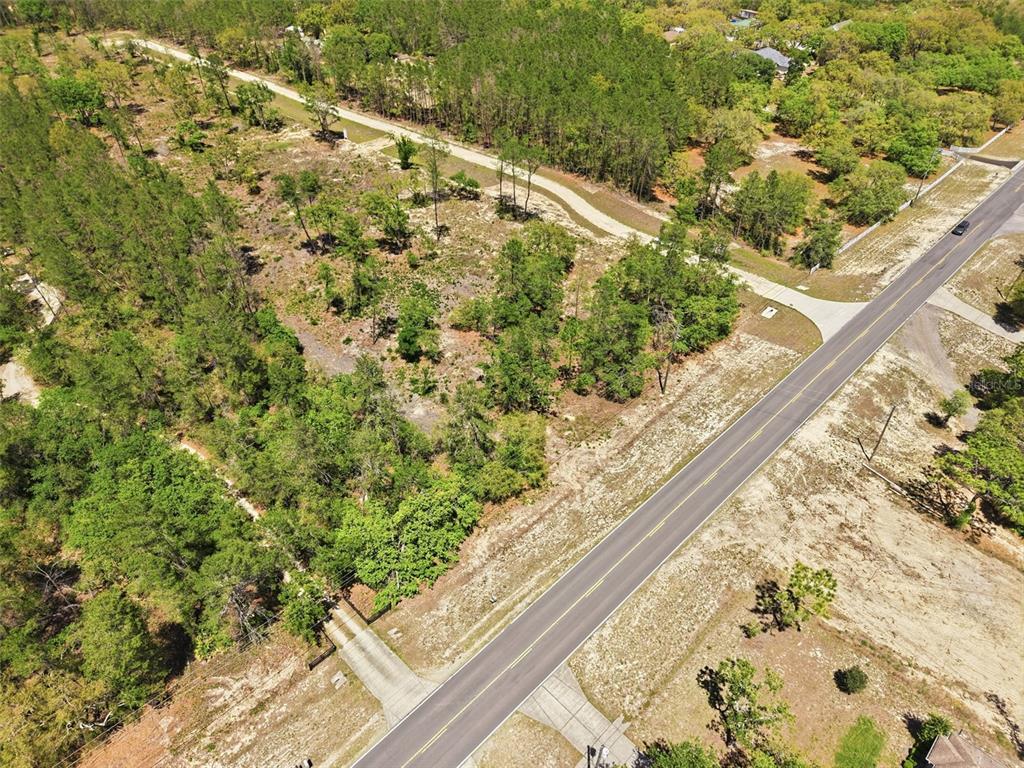 An aerial view shows a paved road running diagonally past a wooded, undeveloped lot — 13183 HAVEN (LOT 1) TRAIL, WEEKI WACHEE, FL