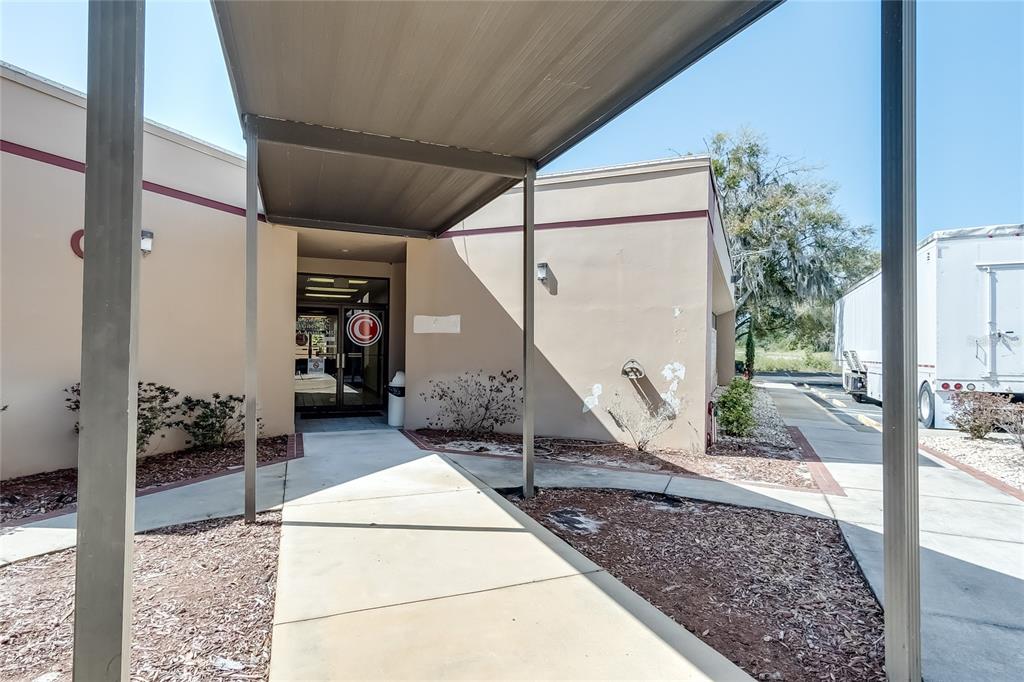 A covered walkway leads to the entrance of a beige commercial building with a glass door — 6801 US 27 HIGHWAY N UNIT C-3, SEBRING, FL