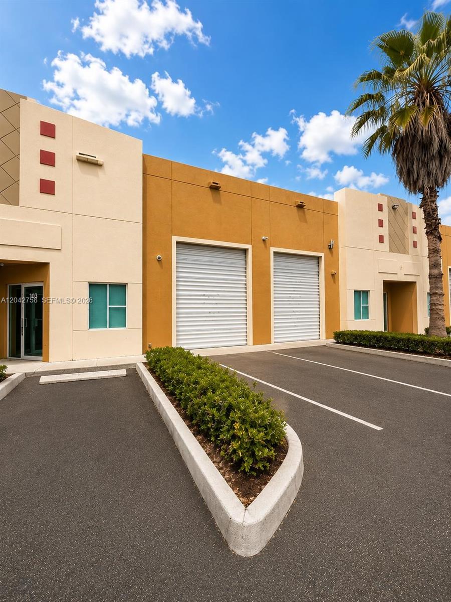 The exterior of a commercial building features two roll-up doors, parking spaces, and landscaping — 9450 NW 58th St, Doral FL 33178, DORAL, FL