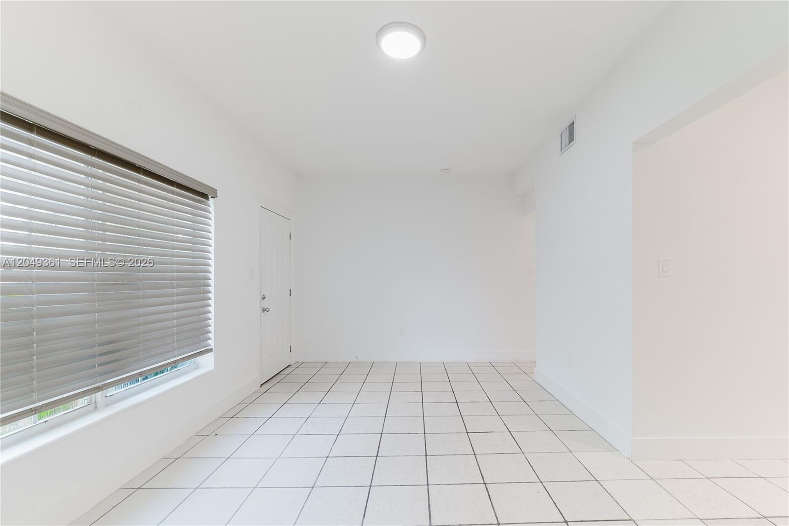 An empty room features white walls, white tile flooring, a window with blinds, and a door — 6130 Flagler St, Hollywood FL 33023, HOLLYWOOD, FL
