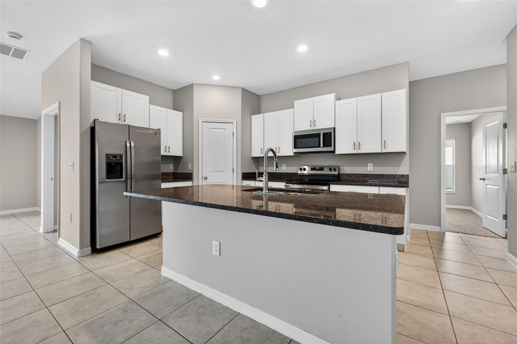 A kitchen features white cabinets, granite countertops, a stainless steel refrigerator, and tile flooring — 13236 JETER CREEK DRIVE, RIVERVIEW, FL