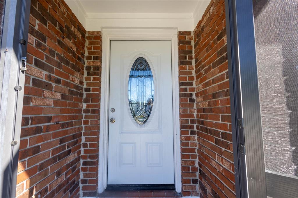 A white front door with an oval glass insert is framed by red brick walls — 724 TRADEWINDS DRIVE, BRANDON, FL
