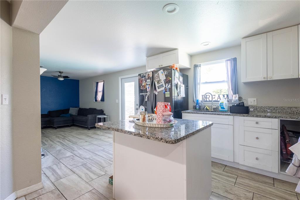 A kitchen with a granite-topped island and white cabinets opens into a living room area — 724 TRADEWINDS DRIVE, BRANDON, FL
