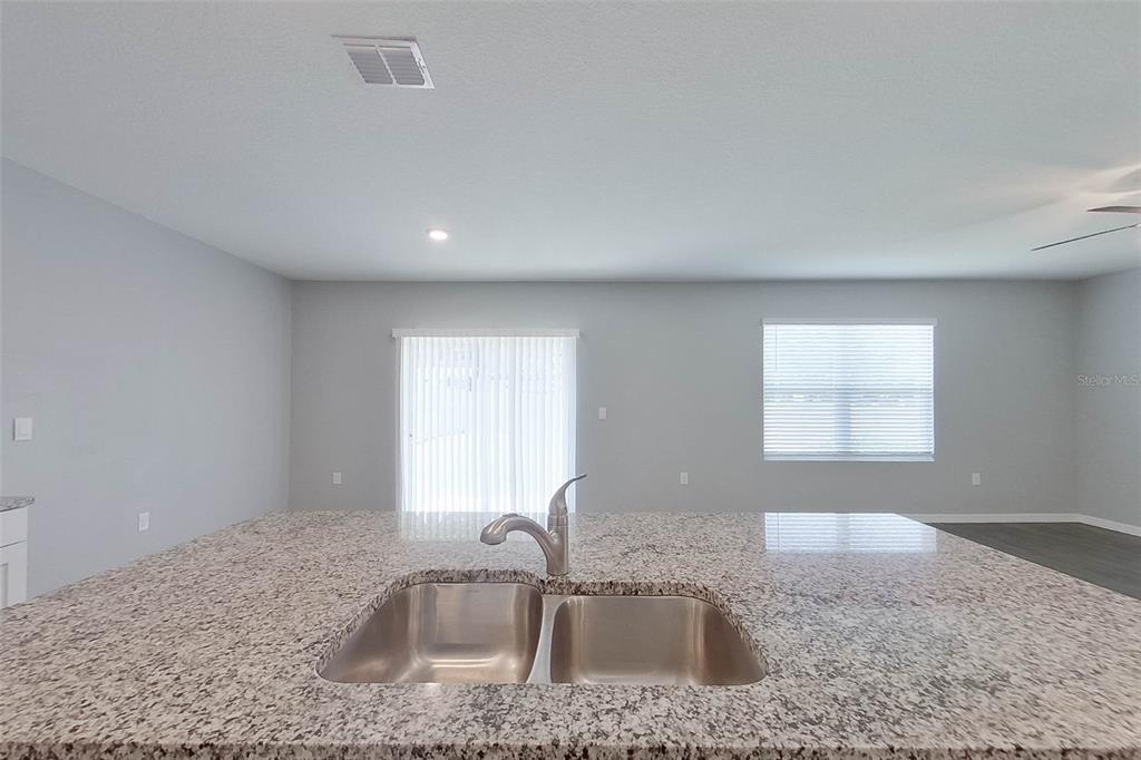 A kitchen island with a double-basin stainless steel sink and granite countertop faces a living area — 32221 EDSON AVE, LEESBURG, FL