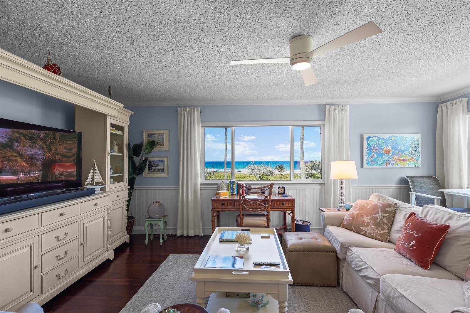 A living room features a white entertainment center, a desk by a window, and ocean views — 250 S Ocean Boulevard # 254, Delray Beach FL 33483, DELRAY BEACH, FL