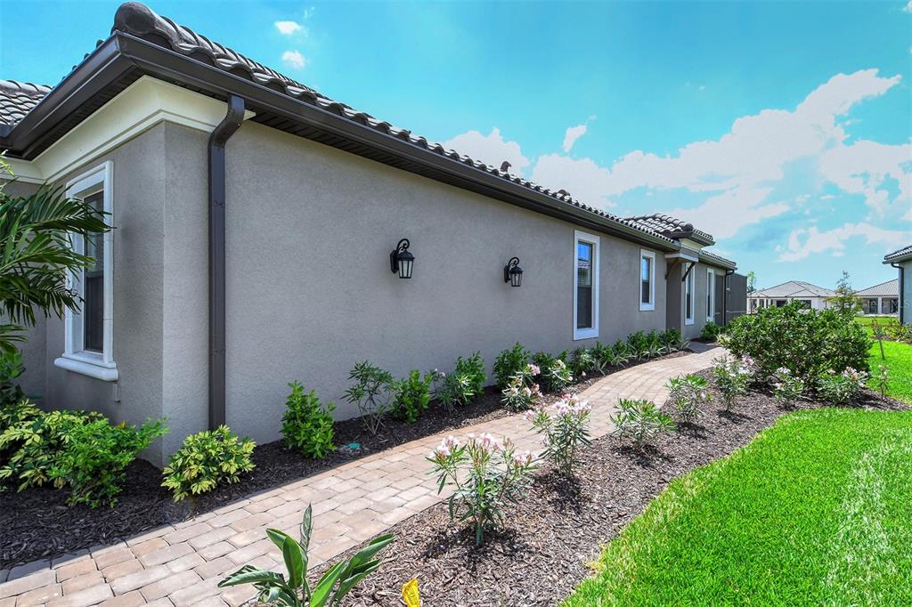 A paved walkway runs alongside the side exterior of a beige house with dark roof tiles — 4708 MOTTA COURT, BRADENTON, FL