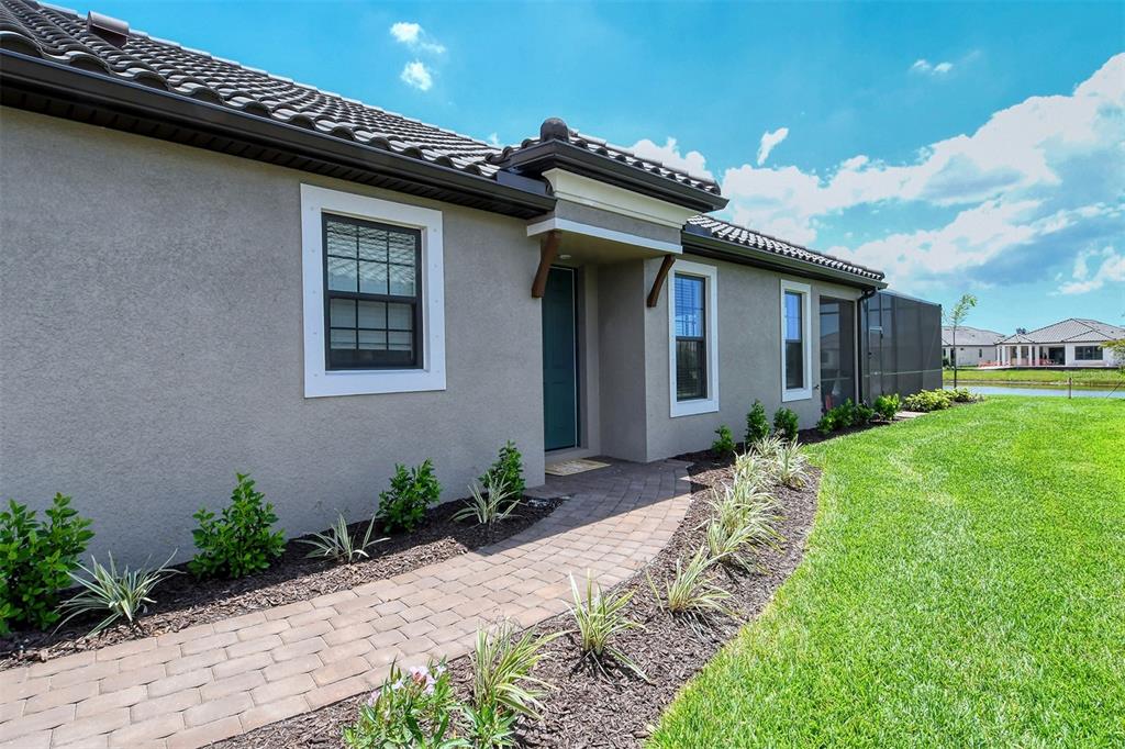 A paved walkway leads to the front entrance of a stucco house with a tiled roof — 4708 MOTTA COURT, BRADENTON, FL