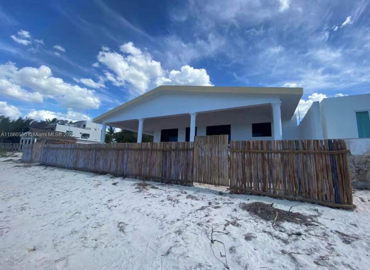 A white house with a covered porch stands behind a tall wooden fence on sand — Calle 18 y 2 Telchak Puerto, Mx, Mx
