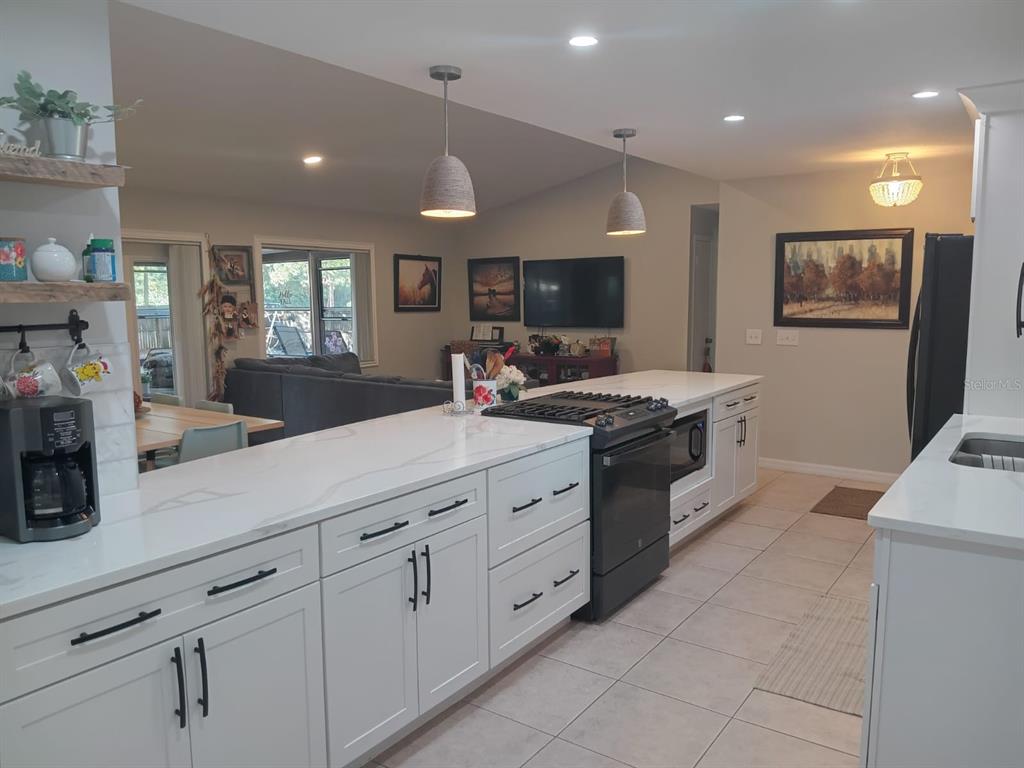 A kitchen features white cabinets, quartz countertops, a gas range, and a view into the living room — 10700 GARDENWOOD ROAD, ORLANDO, FL