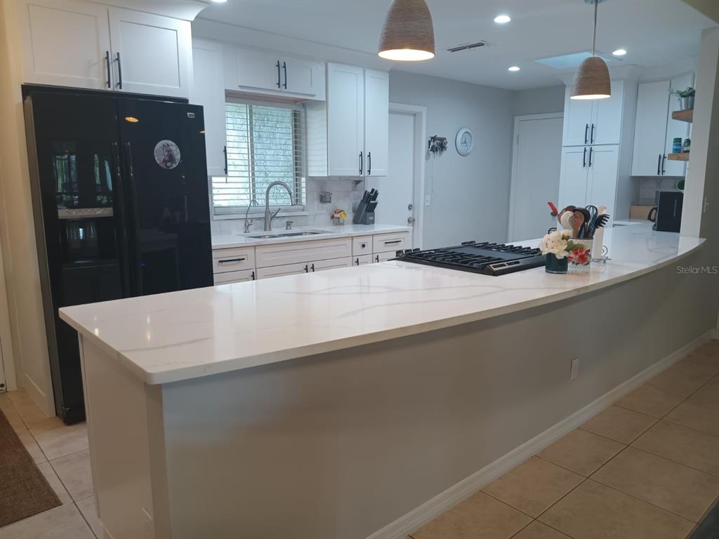 A kitchen features white cabinets, a large quartz island with a cooktop, and black appliances — 10700 GARDENWOOD ROAD, ORLANDO, FL