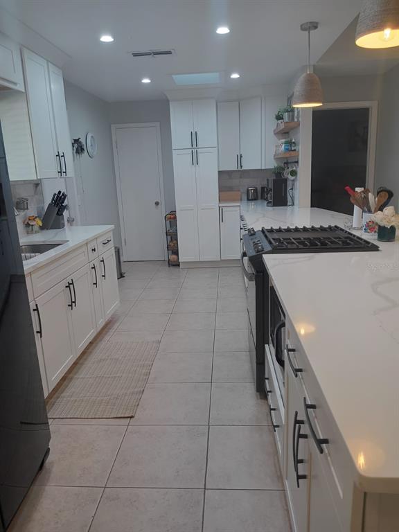 A modern kitchen features white cabinets, light countertops, a gas range, and tiled flooring — 10700 GARDENWOOD ROAD, ORLANDO, FL