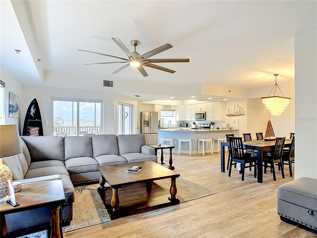 An open-concept living and dining area features a sectional sofa, kitchen island, and wood flooring — 5300 S ATLANTIC AVENUE UNIT 5-301, NEW SMYRNA BEACH, FL