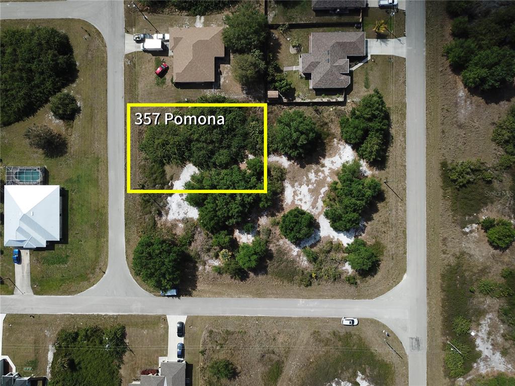 This aerial view shows a vacant, partially wooded residential lot in a suburban neighborhood — 357 POMONA STREET, LEHIGH ACRES, FL