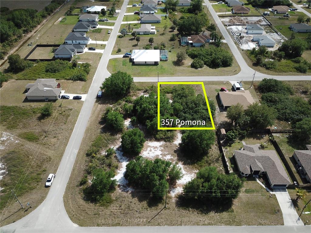 An aerial view shows a vacant, tree-covered residential lot outlined in yellow within a neighborhood — 357 POMONA STREET, LEHIGH ACRES, FL