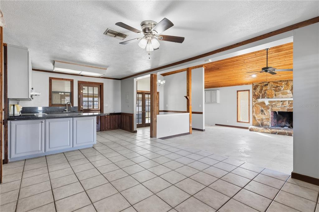 A kitchen with tile floors and gray cabinets opens into a living room with stone fireplace — 10301 TRAIL RIDGE LANE, TAMPA, FL
