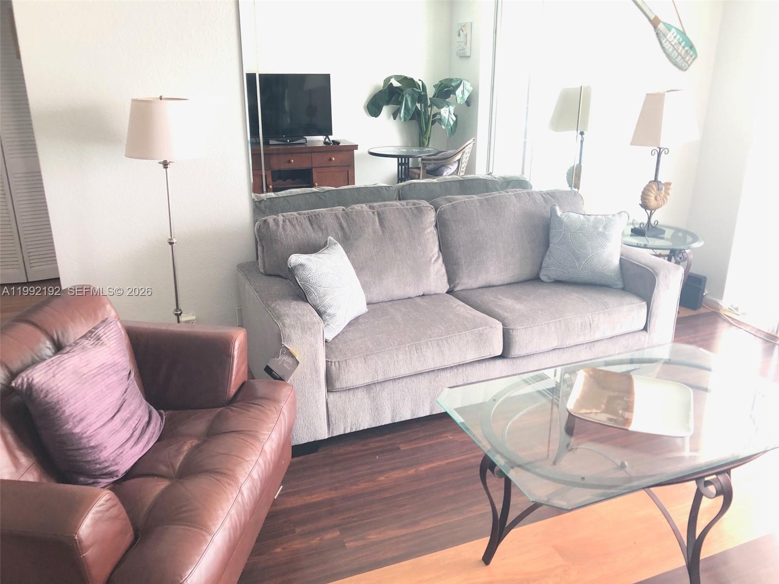 A living room features a gray sofa, a brown leather armchair, and a glass coffee table — 3901 S Ocean Dr # 15C, Hollywood FL 33019, HOLLYWOOD, FL