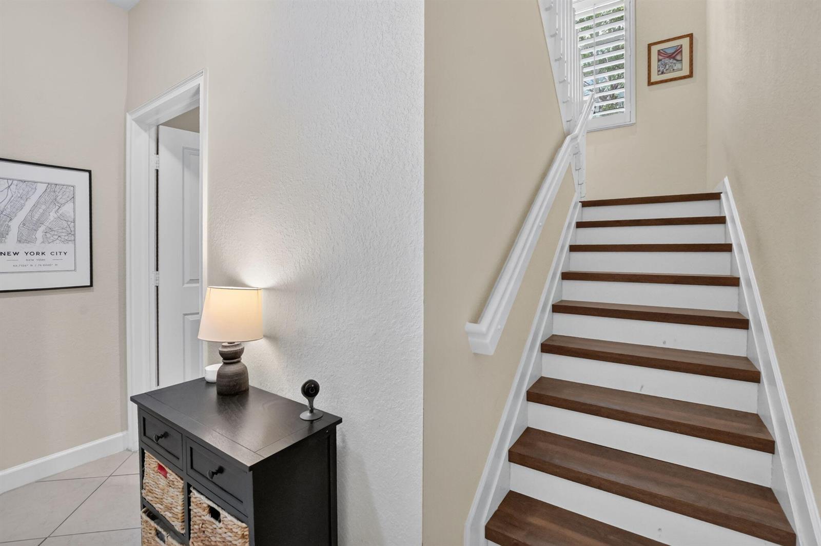 A staircase with dark wood treads and white risers sits beside a small entryway console — 27 NW Hawthorne Place, Boca Raton FL 33432, BOCA RATON, FL