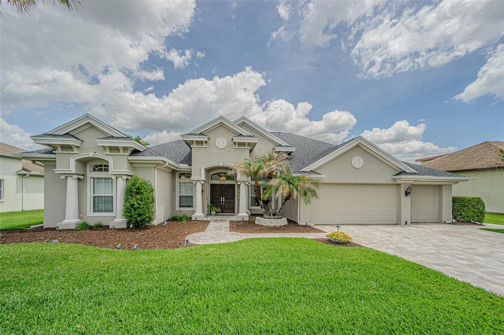 A single-story suburban house with a beige stucco exterior, a three-car garage, and a lawn — 26731 WINGED ELM DRIVE, WESLEY CHAPEL, FL