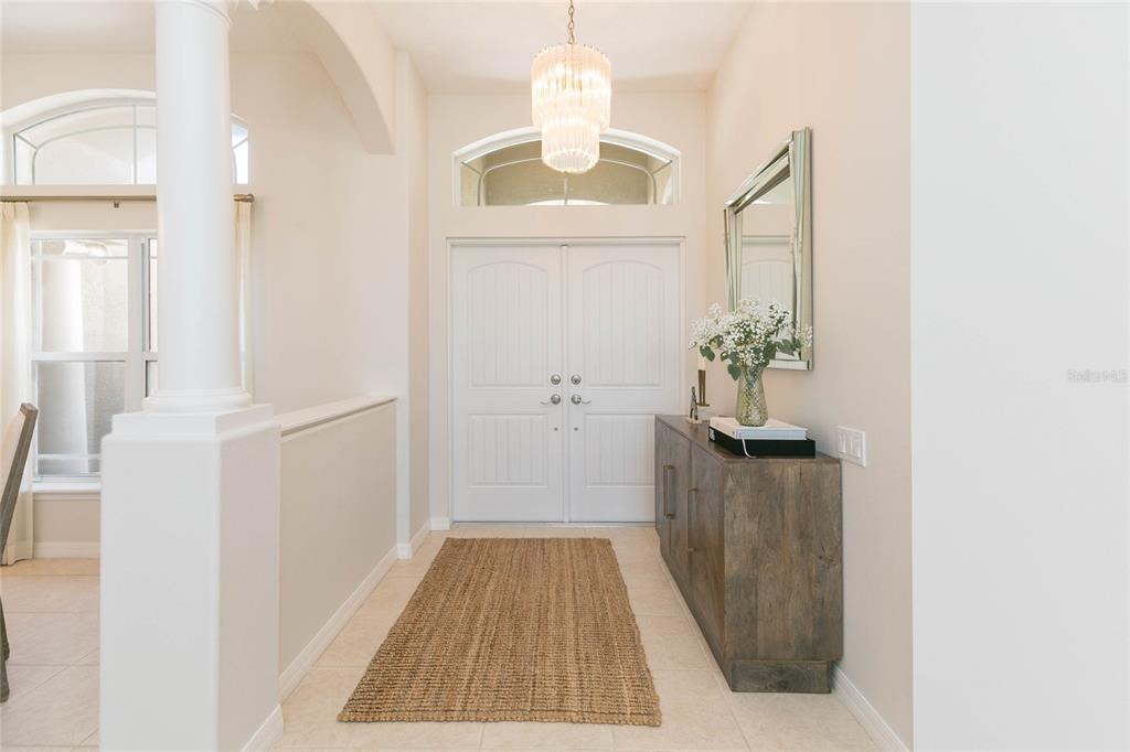 A bright entryway features double doors, a crystal chandelier, and a wooden console table — 26731 WINGED ELM DRIVE, WESLEY CHAPEL, FL