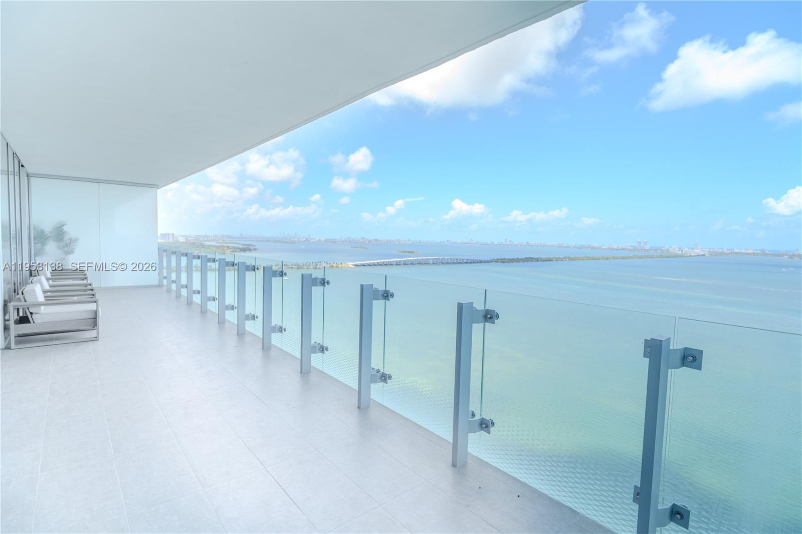 A wide balcony with glass railings overlooks a large body of water and a city — 700 NE 26th Ter # 2602, Miami FL 33137, MIAMI, FL