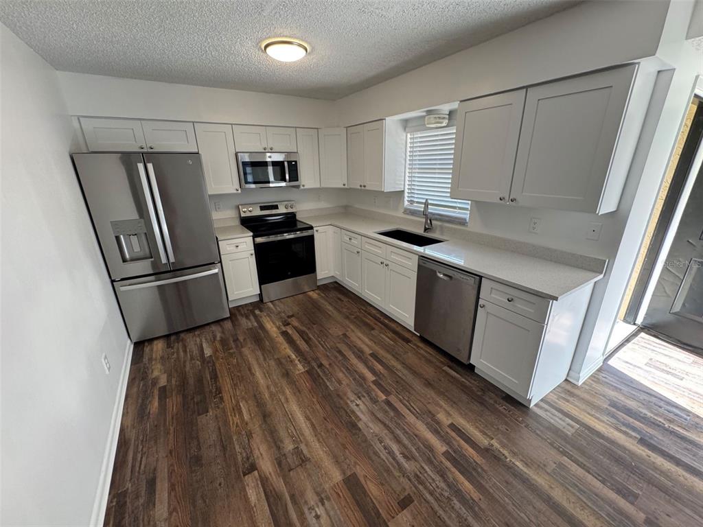 A kitchen features white cabinets, stainless steel appliances, light countertops, and dark wood-look flooring — 4851 16TH STREET, ZEPHYRHILLS, FL