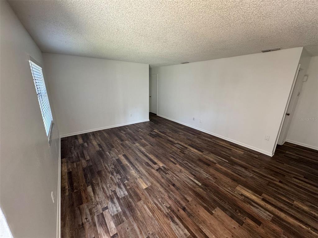 An empty room features white walls, a textured ceiling, and dark wood-look plank flooring — 4851 16TH STREET, ZEPHYRHILLS, FL