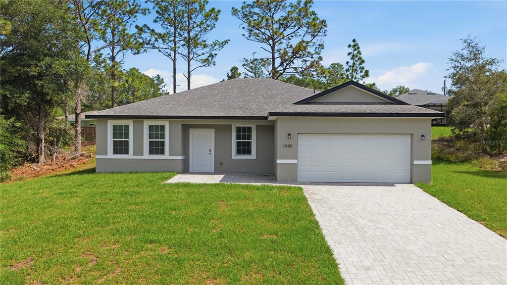 A single-story house with a gray stucco exterior, a white garage door, and a paved driveway — 1985 W CORRINE STREET, DUNNELLON, FL
