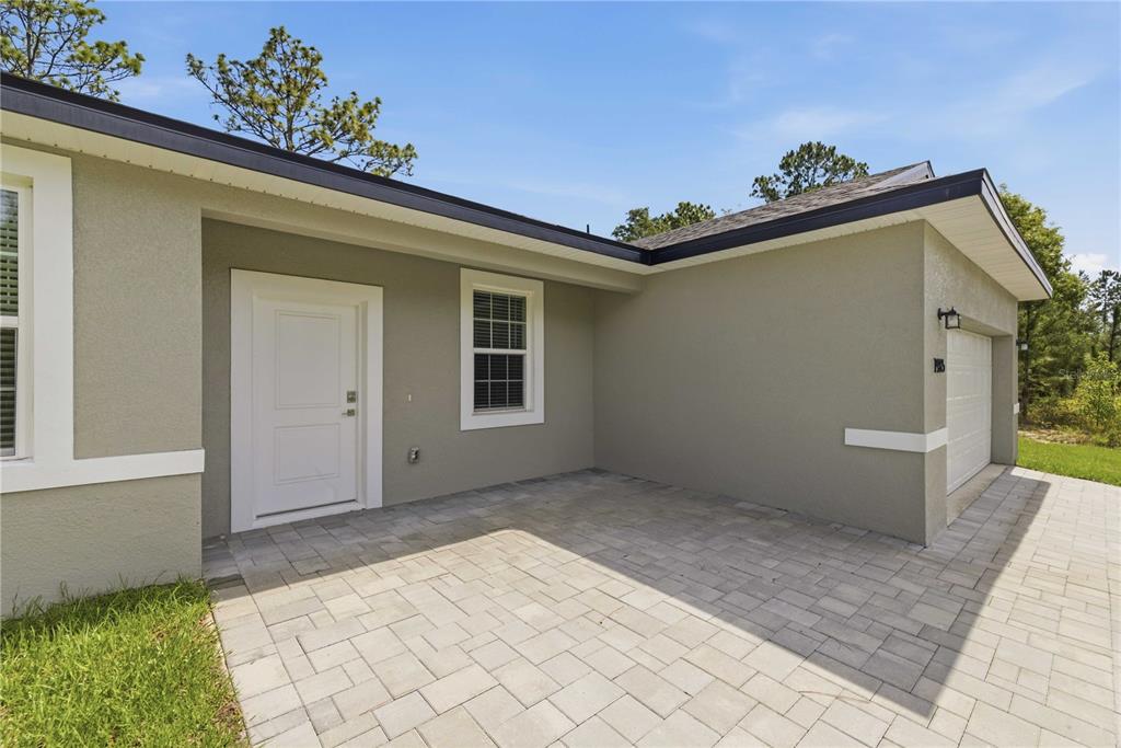 A paved walkway leads to the front entrance and garage of a tan stucco house — 1985 W CORRINE STREET, DUNNELLON, FL