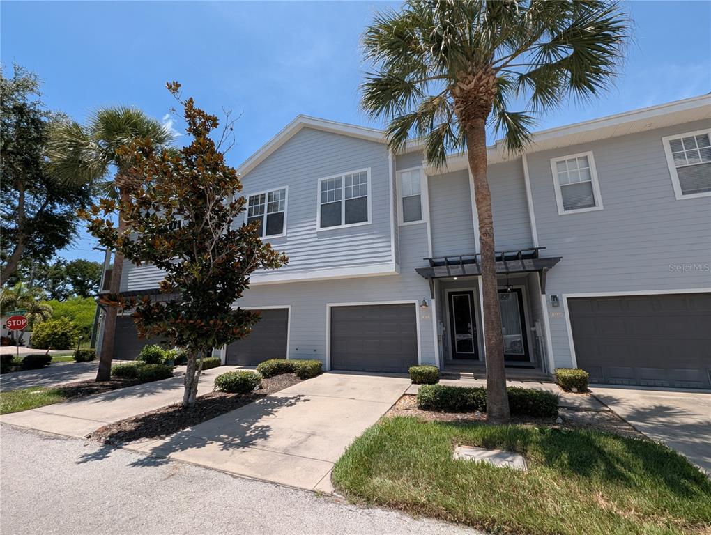 A two-story townhouse with light blue siding, gray garage doors, and palm trees — 8319 KING BLOSSOM COURT, TAMPA, FL