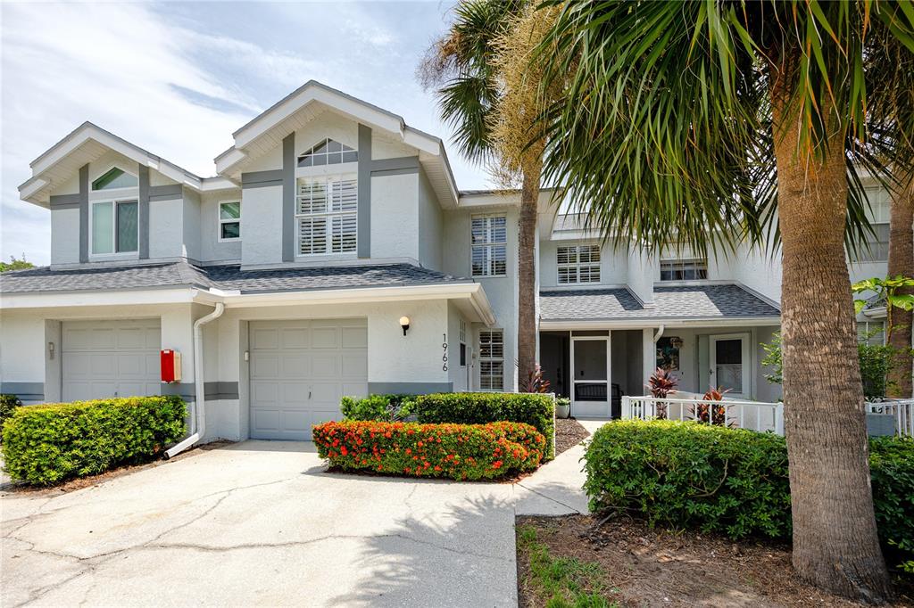 A two-story townhouse exterior with a gray garage, white siding, and a palm tree — 1966 PLANTATION BOULEVARD, CLEARWATER, FL