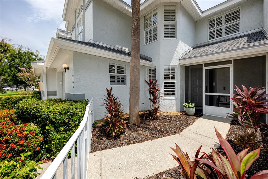 The exterior of a two-story house features a white stucco facade, a palm tree, and landscaping — 1966 PLANTATION BOULEVARD, CLEARWATER, FL
