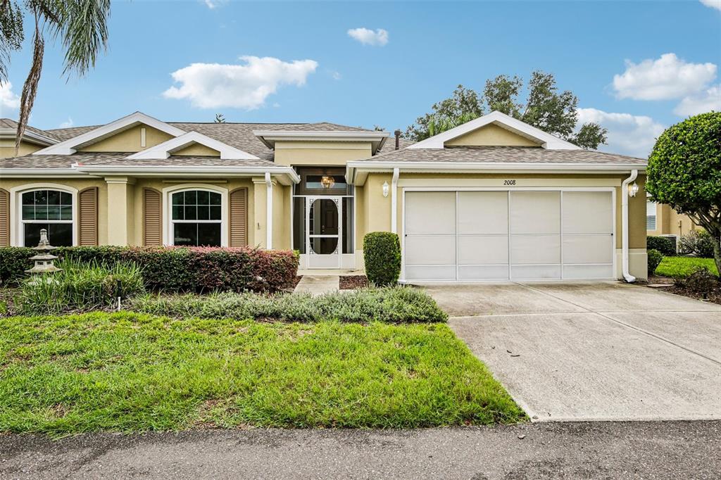 A single-story house with a beige exterior, a two-car garage, and a front entryway screen door — 2008 GRANTHAM GREENS DRIVE, SUN CITY CENTER, FL