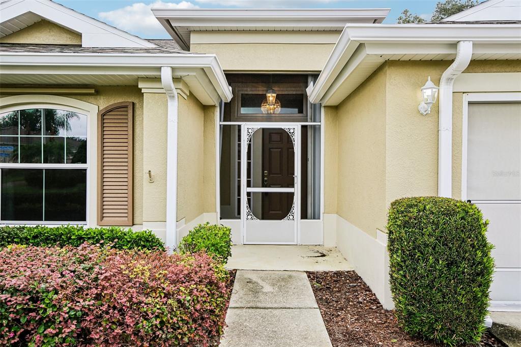 The exterior of a house features a concrete walkway leading to a white screen door — 2008 GRANTHAM GREENS DRIVE, SUN CITY CENTER, FL