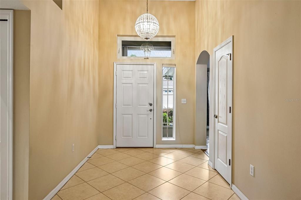 A bright entryway features tan tile flooring, a white front door, and a crystal chandelier — 2008 GRANTHAM GREENS DRIVE, SUN CITY CENTER, FL
