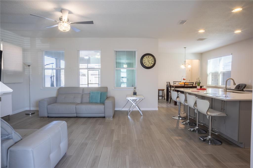 An open-concept living room and kitchen featuring light wood floors, gray furniture, and bar seating — 16461 OLIVE HILL DRIVE, WINTER GARDEN, FL