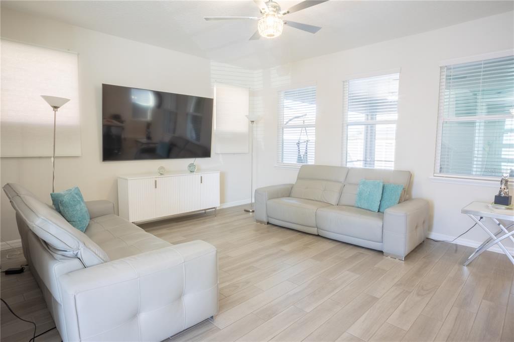 A living room with light gray tile flooring, two leather sofas, and a wall-mounted television — 16461 OLIVE HILL DRIVE, WINTER GARDEN, FL