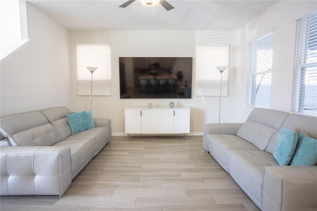 A living room features two gray sofas, a wall-mounted television, and a white media console — 16461 OLIVE HILL DRIVE, WINTER GARDEN, FL