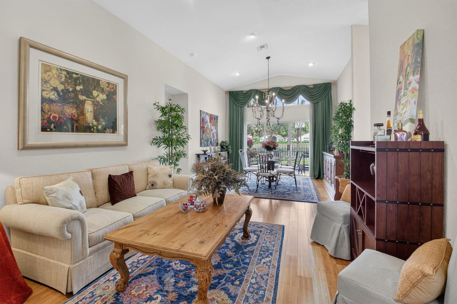 A living and dining room with hardwood floors, vaulted ceilings, and a large area rug — 6877 Castlemaine Avenue, Boynton Beach FL 33437, BOYNTON BEACH, FL