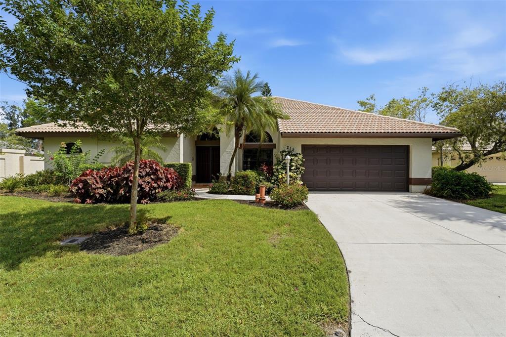 A single-story house with a brown tile roof, a two-car garage, and a landscaped yard — 215 CARRIAGE HOUSE LANE UNIT 215, NOKOMIS, FL