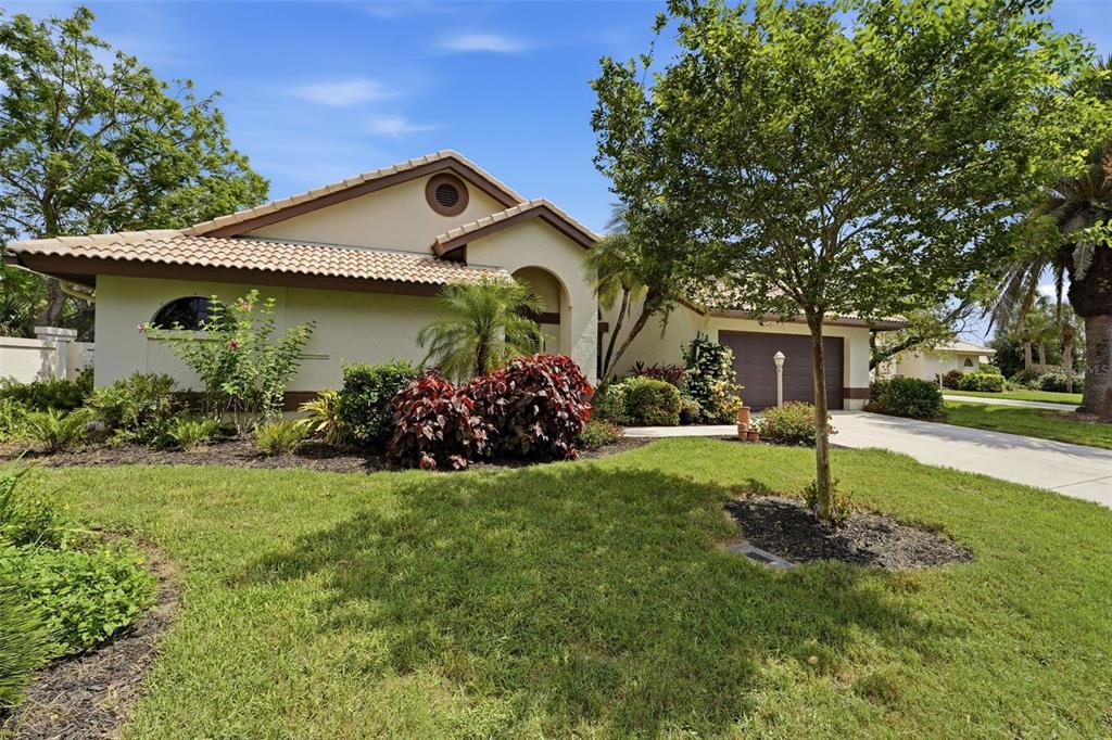A single-story house with a tiled roof, beige stucco exterior, and a front lawn — 215 CARRIAGE HOUSE LANE UNIT 215, NOKOMIS, FL