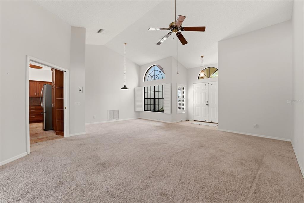 A spacious living room features high vaulted ceilings, beige carpeting, and a large arched window — 215 CARRIAGE HOUSE LANE UNIT 215, NOKOMIS, FL