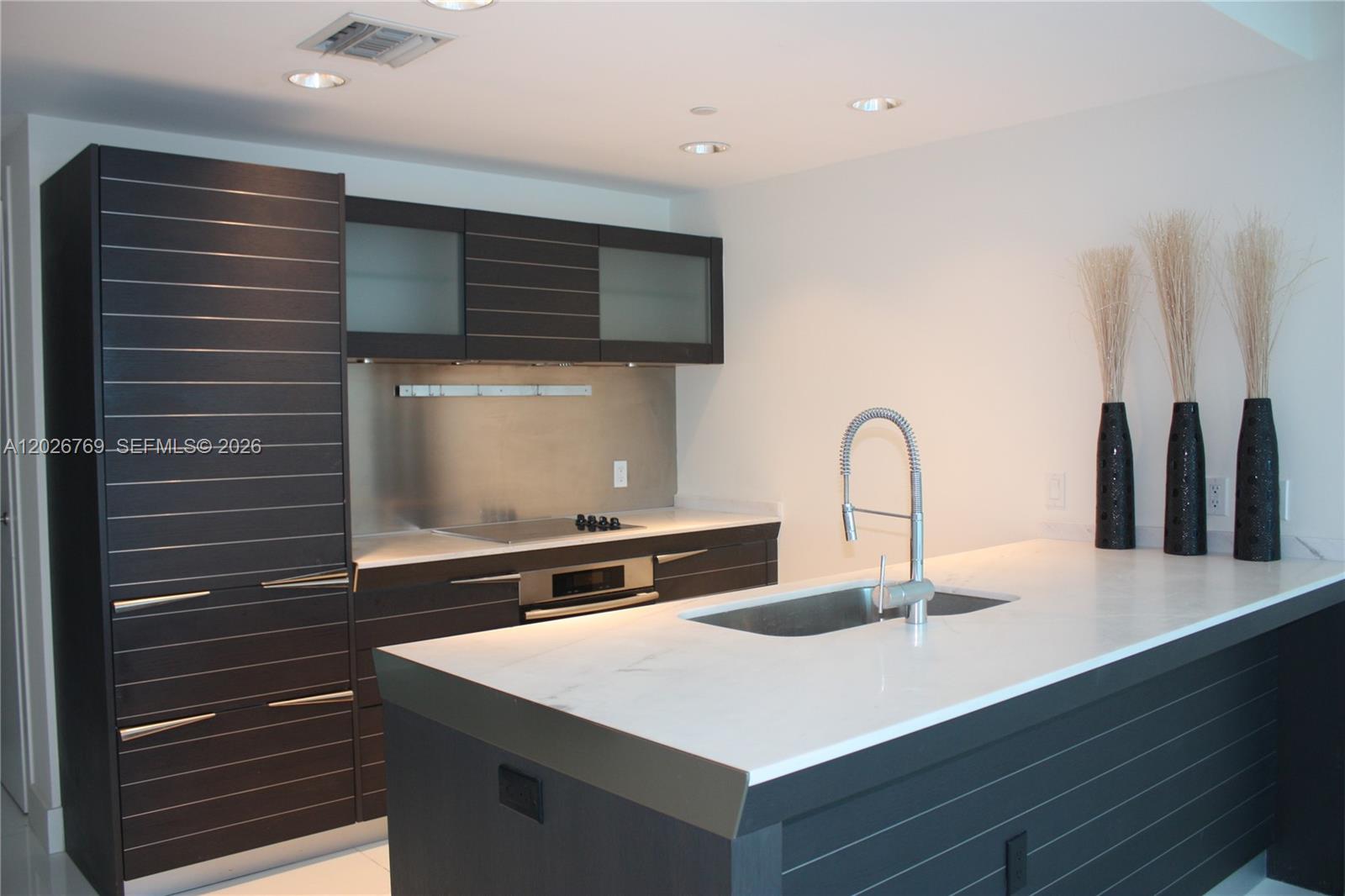 A modern kitchen features dark horizontal-slatted cabinetry, white countertops, and a central island with sink — 200 Biscayne Boulevard Way # 4211, Miami FL 33131, MIAMI, FL