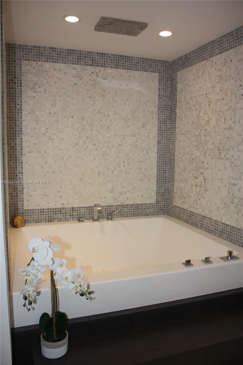 A white soaking tub is set against a wall with gray and white mosaic tiles — 200 Biscayne Boulevard Way # 4211, Miami FL 33131, MIAMI, FL